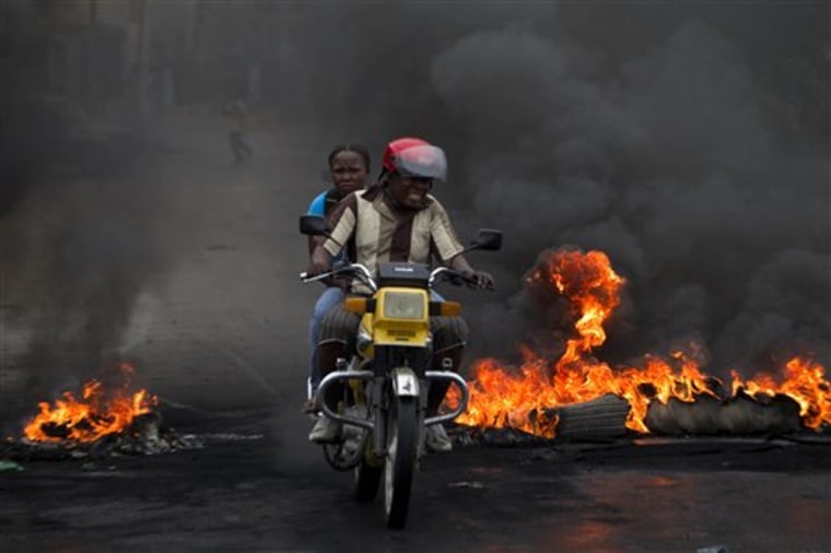 A man drives a motorcycle past a barricade of burning tires in Port-au-Prince, Haiti, on Thursday. 